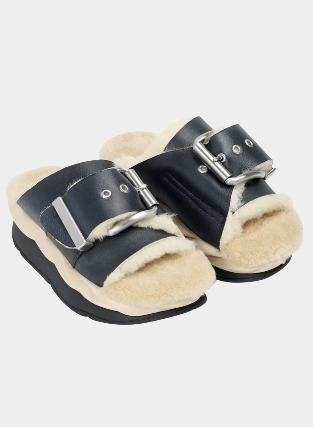 Black and beige slip-on shoes with buckle details on a light gray background